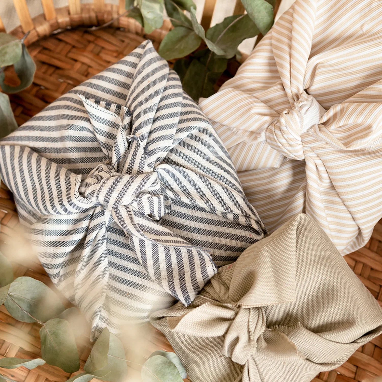 Striped fabric bundles on a woven surface with green leaves.