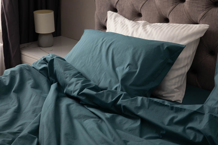 Modern bedroom with a neatly made bed featuring teal bedding, white striped pillows, and a tufted headboard, with a bedside lamp on a white nightstand