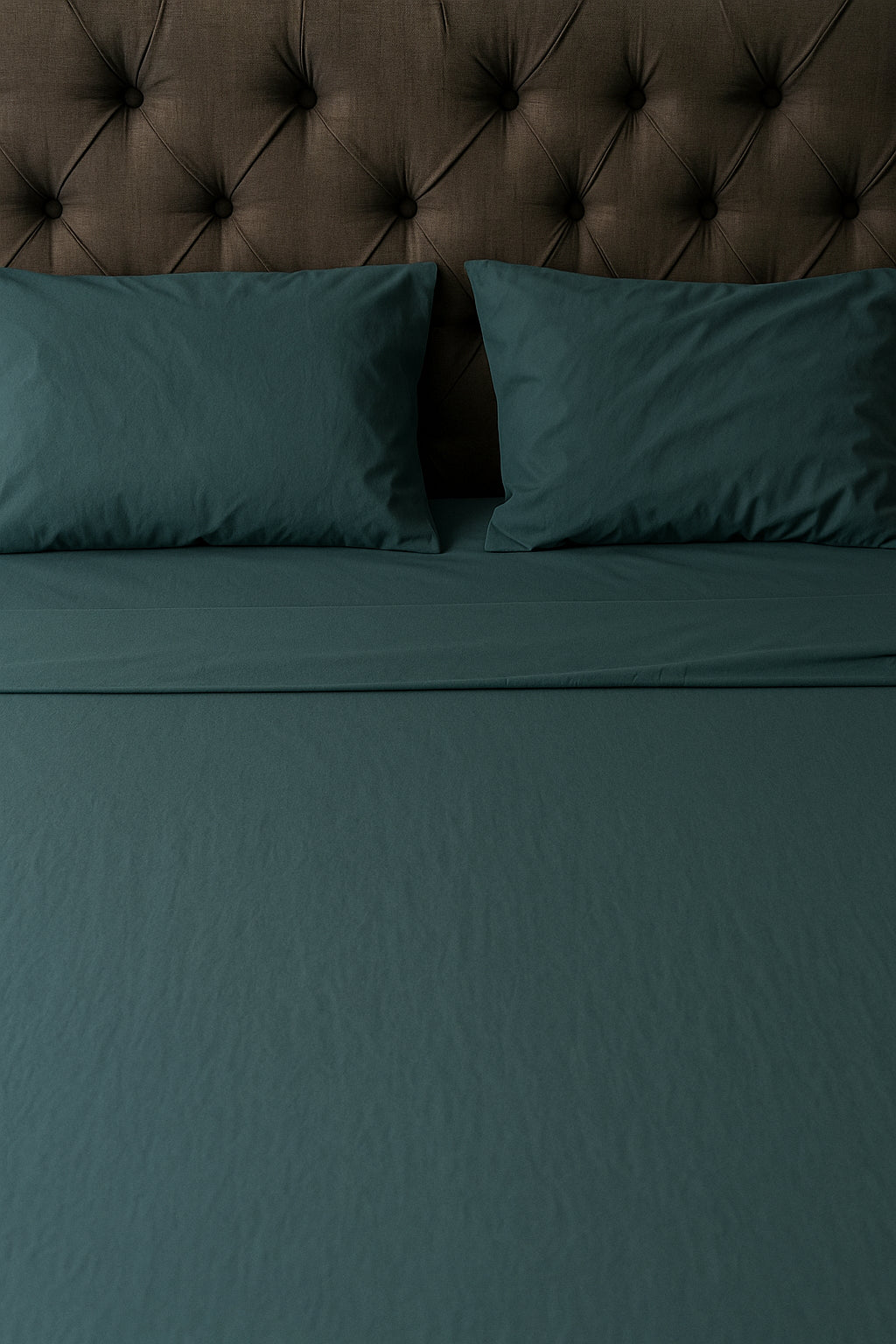 Minimalist bedding in a rich greenish-blue tone against a dark tufted headboard, showcasing a smooth and refined fabric finish