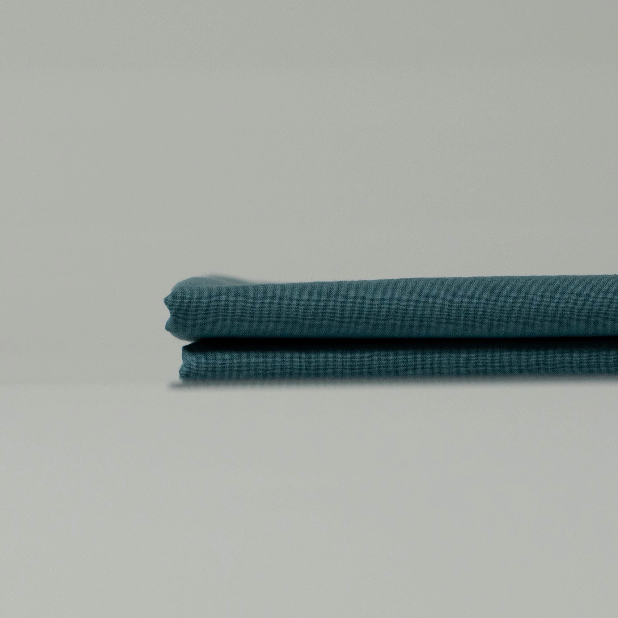 Neatly folded deep cyan fabric with a soft matte texture, showcasing refined tones and handcrafted character
