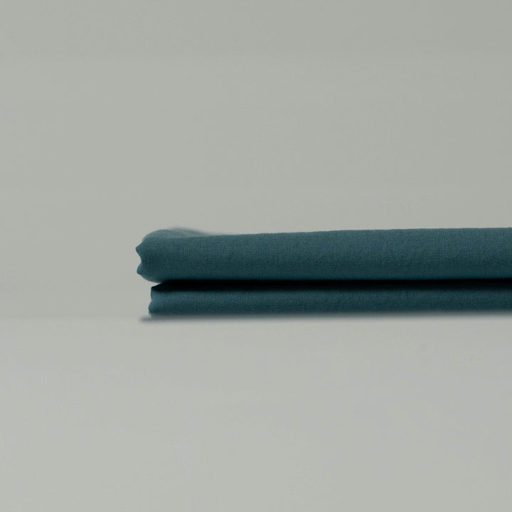 Neatly folded deep cyan fabric with a soft matte texture, showcasing refined tones and handcrafted character