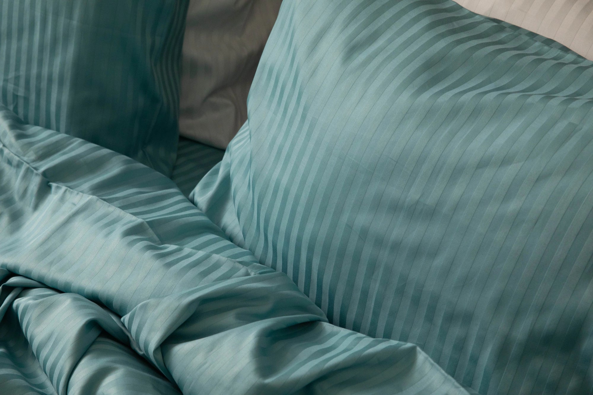 Handcrafted bedding in a dusky aqua sateen weave, featuring subtle stripes and softly layered textures that evoke artisanal comfort and refined luxury