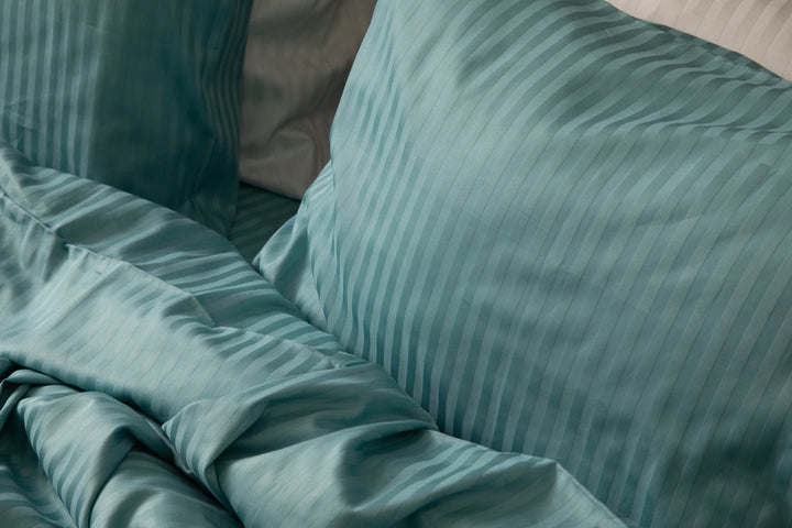 Handcrafted bedding in a dusky aqua sateen weave, featuring subtle stripes and softly layered textures that evoke artisanal comfort and refined luxury