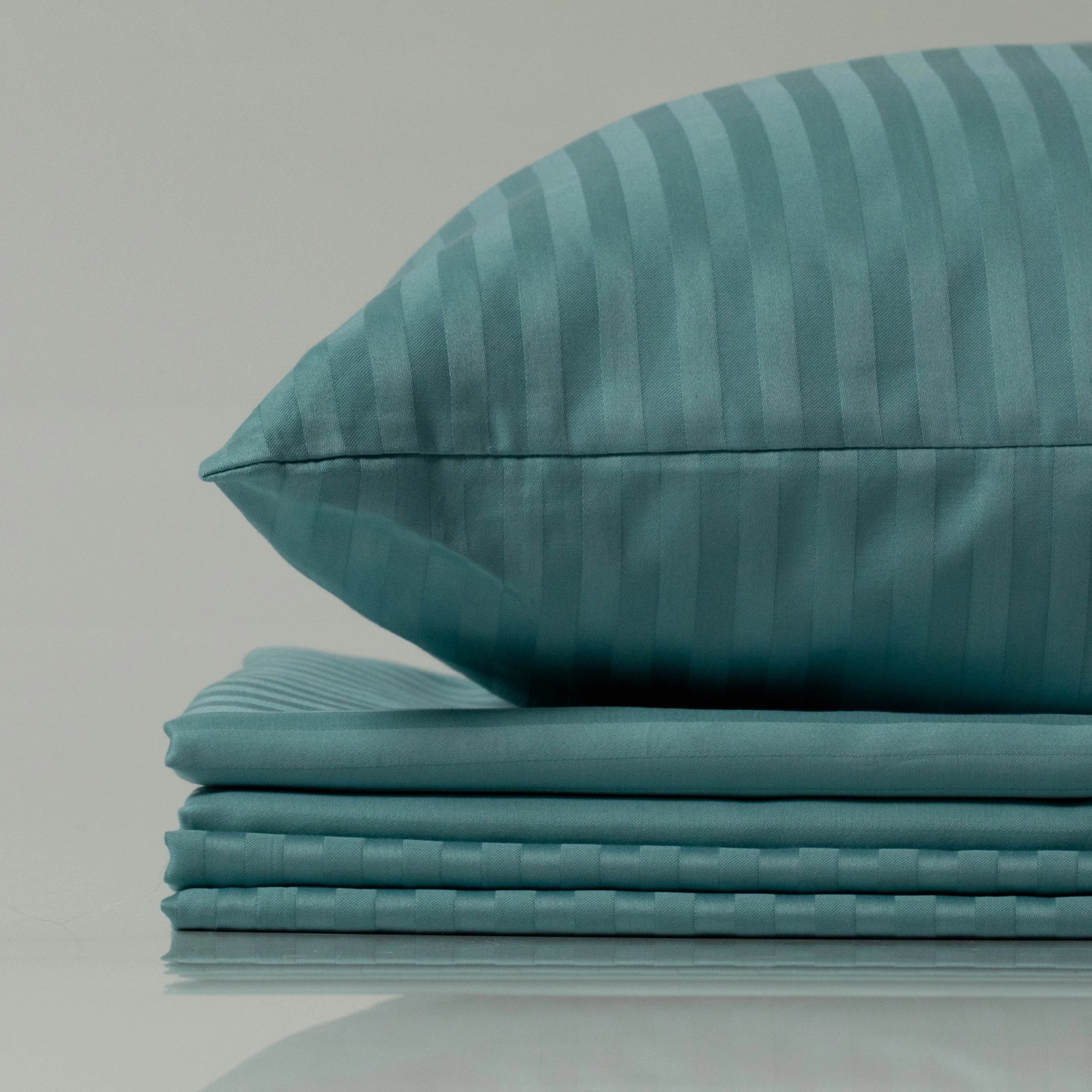 Teal Supreme Rest pillow and folded bedding set with subtle stripe detailing, highlighting custom-made, eco-friendly luxury