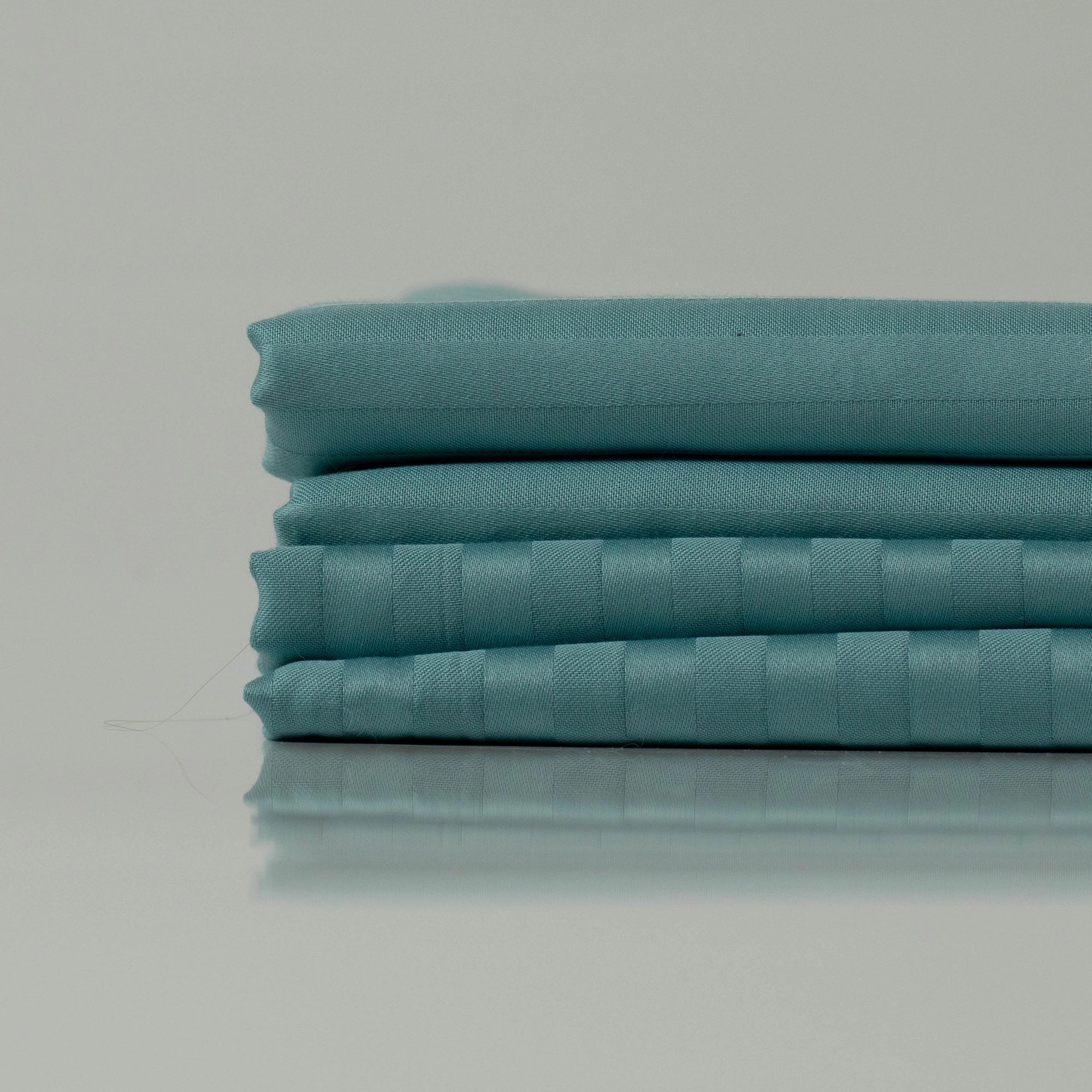 Neatly folded ocean blue bedding with a refined stripe weave, showcasing a handcrafted finish and luxurious fabric texture