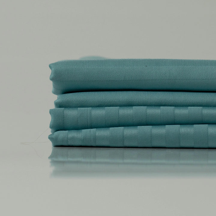 Neatly folded ocean blue bedding with a refined stripe weave, showcasing a handcrafted finish and luxurious fabric texture