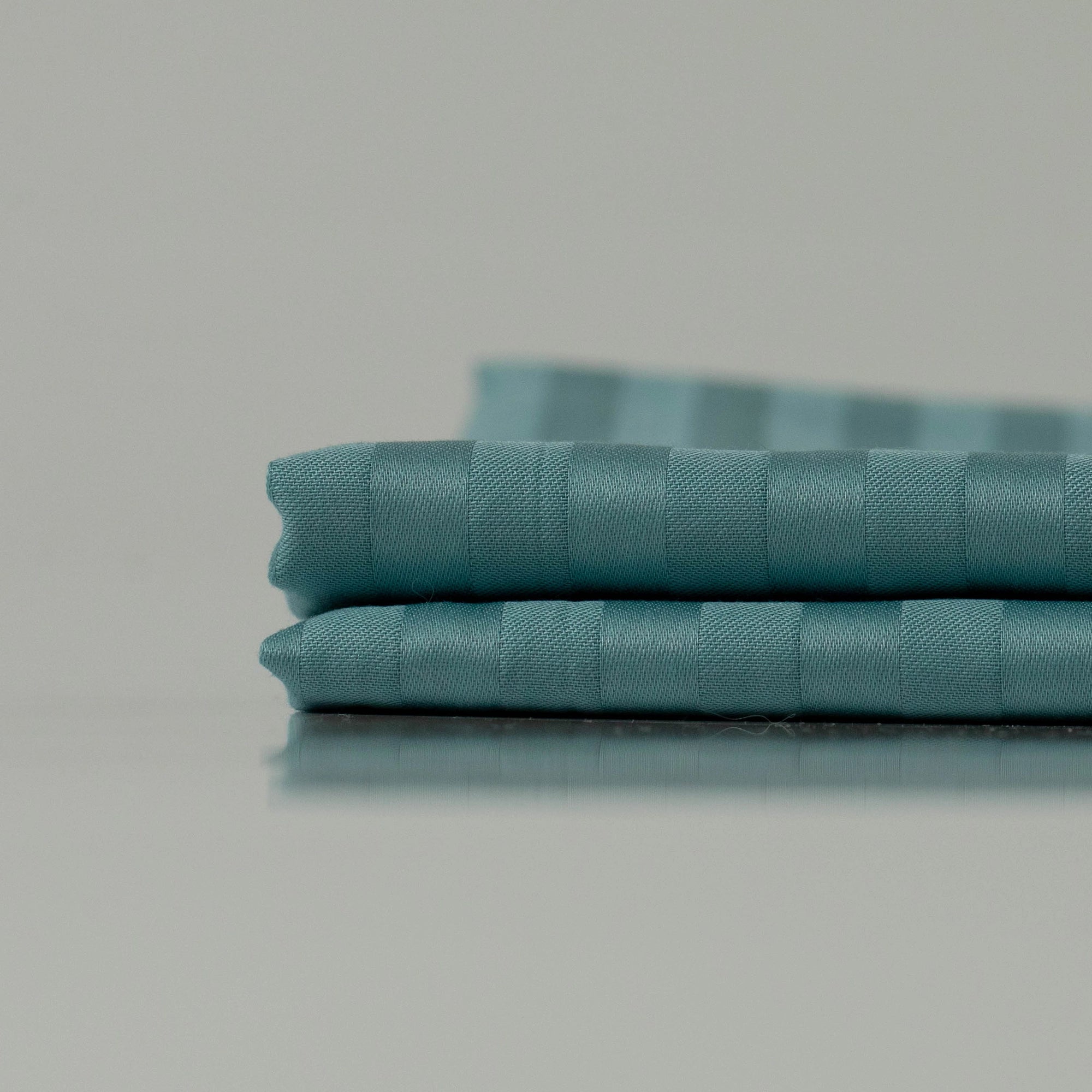 Stacked deep cyan fabric with subtle stripes, showcasing handcrafted precision and a luxuriously smooth finish