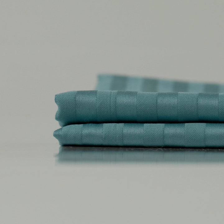 Stacked deep cyan fabric with subtle stripes, showcasing handcrafted precision and a luxuriously smooth finish