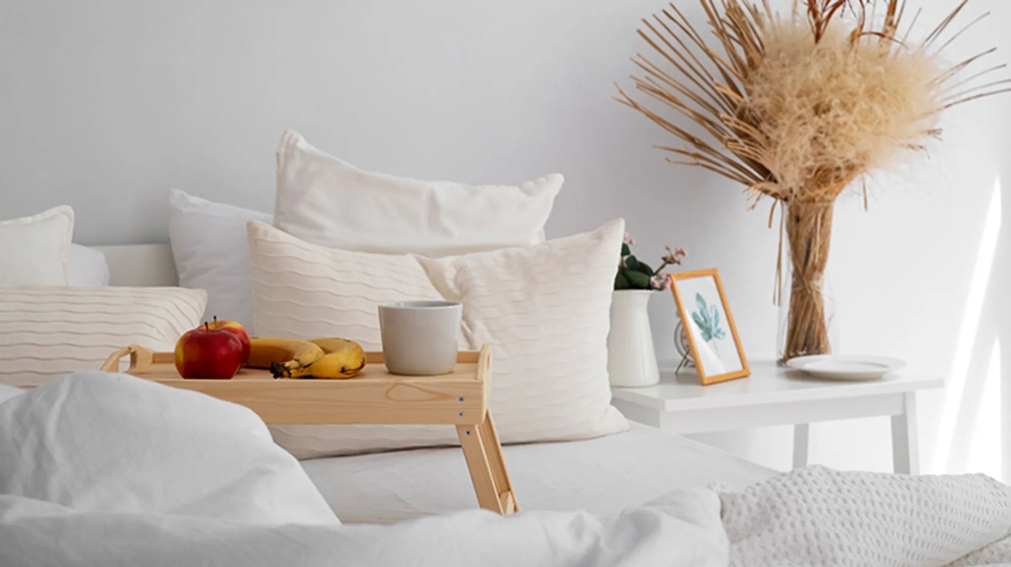 Bedroom with white bedding, pillows, and a small table with fruit and decor.