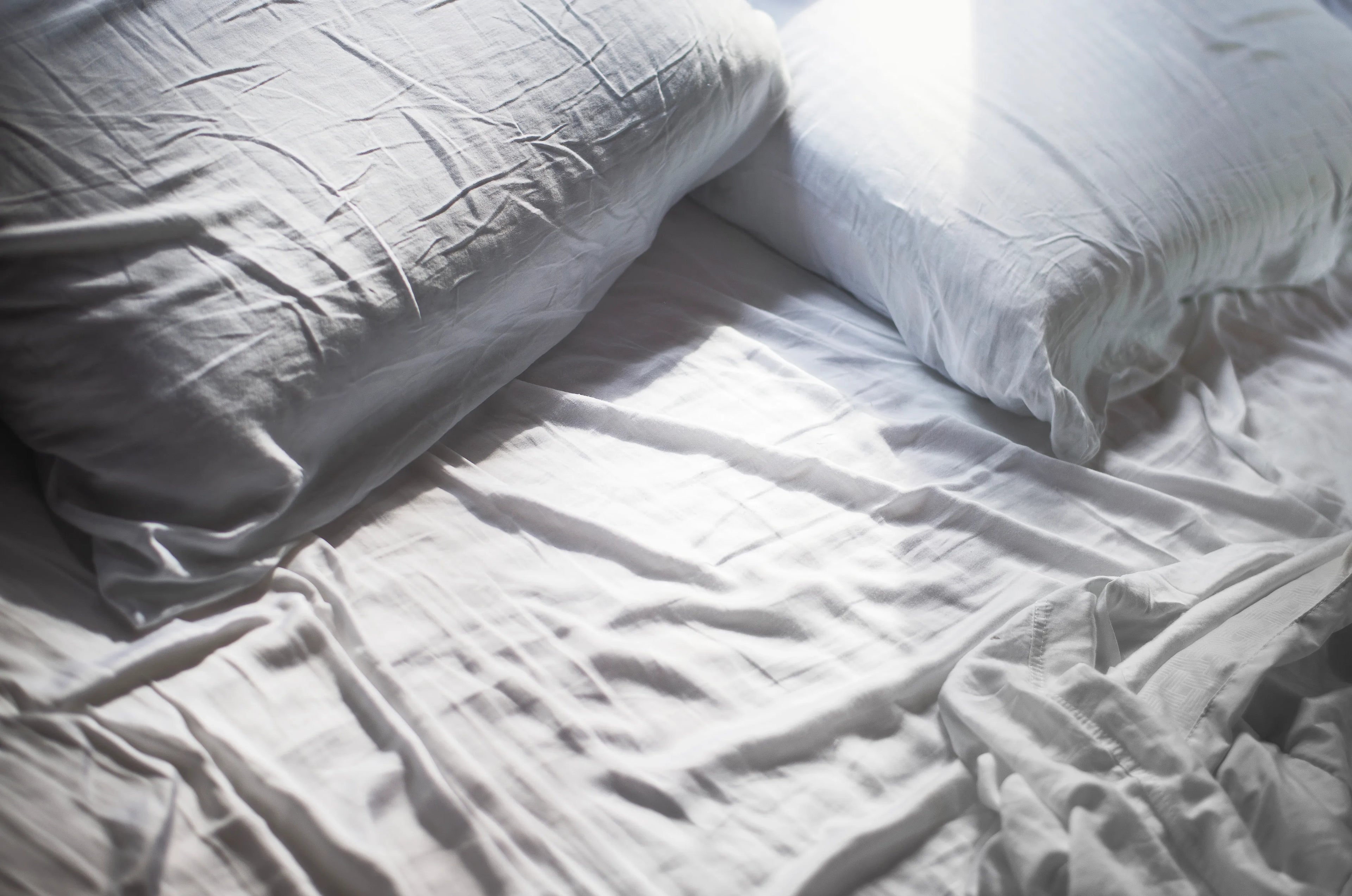 Crumpled white sheets and pillows on an unmade bed in soft natural light.